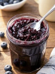 Jar of blueberry jam with spoon and striped napkin.
