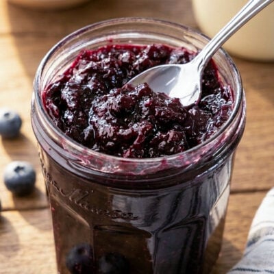 Jar of blueberry jam with spoon and striped napkin.