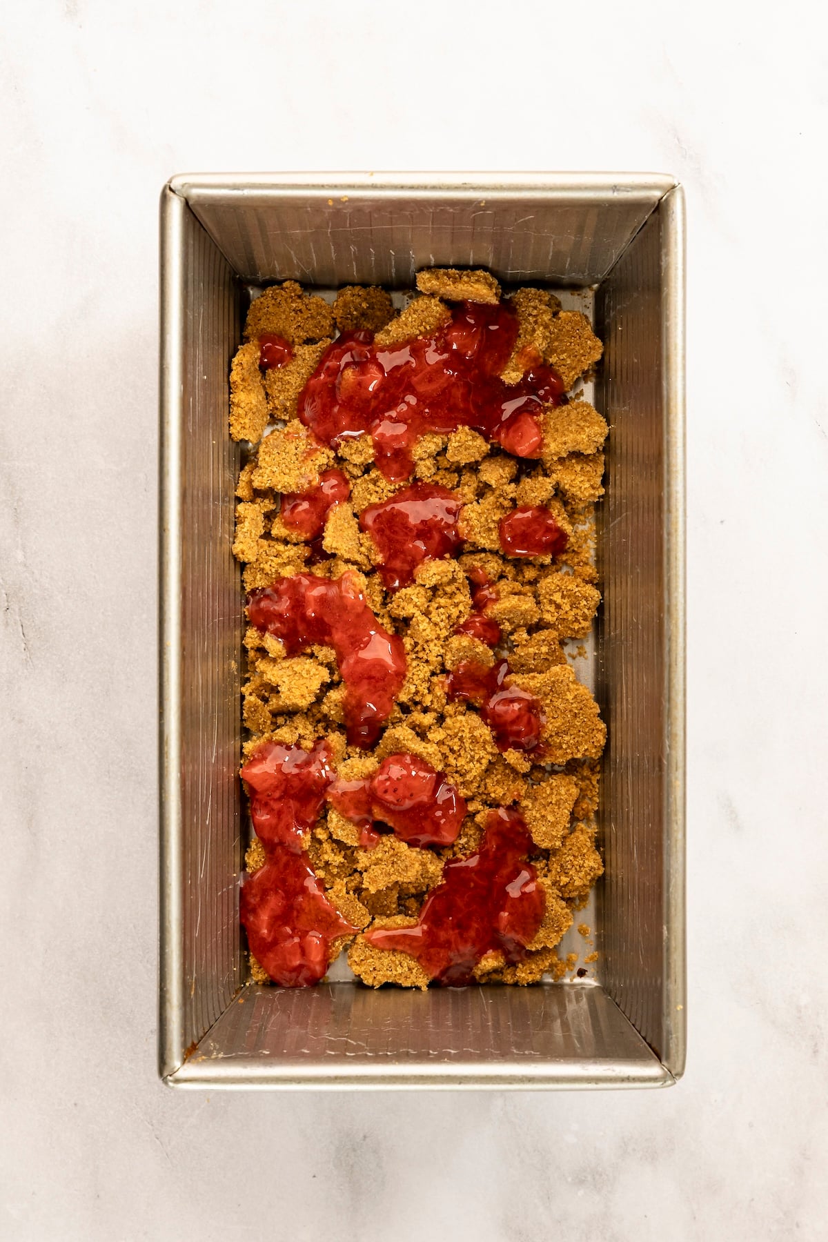 9 x 5 inch loaf pan with strawberry sauce drizzled over crust crumbles