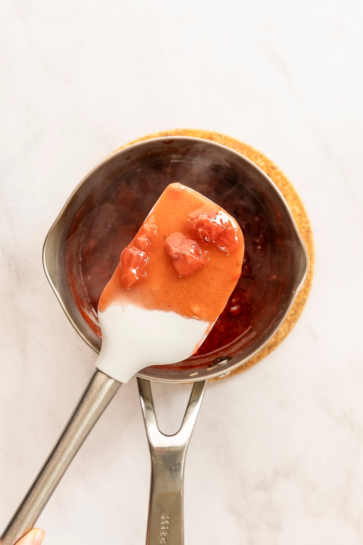 small saucepan and spatula with cooked strawberry mixture