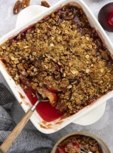 Plum crisp in baking dish with small serving in bowl nearby.