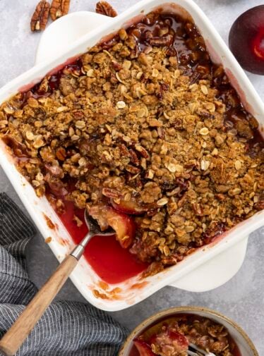Plum crisp in baking dish with small serving in bowl nearby.