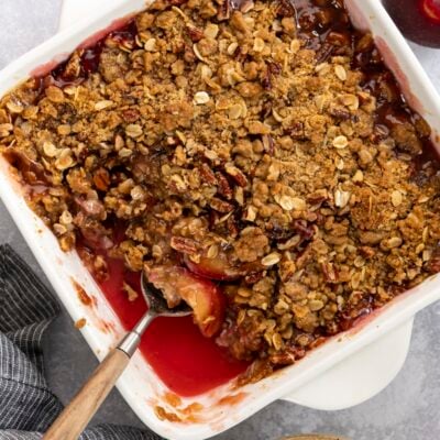 Plum crisp in baking dish with small serving in bowl nearby.