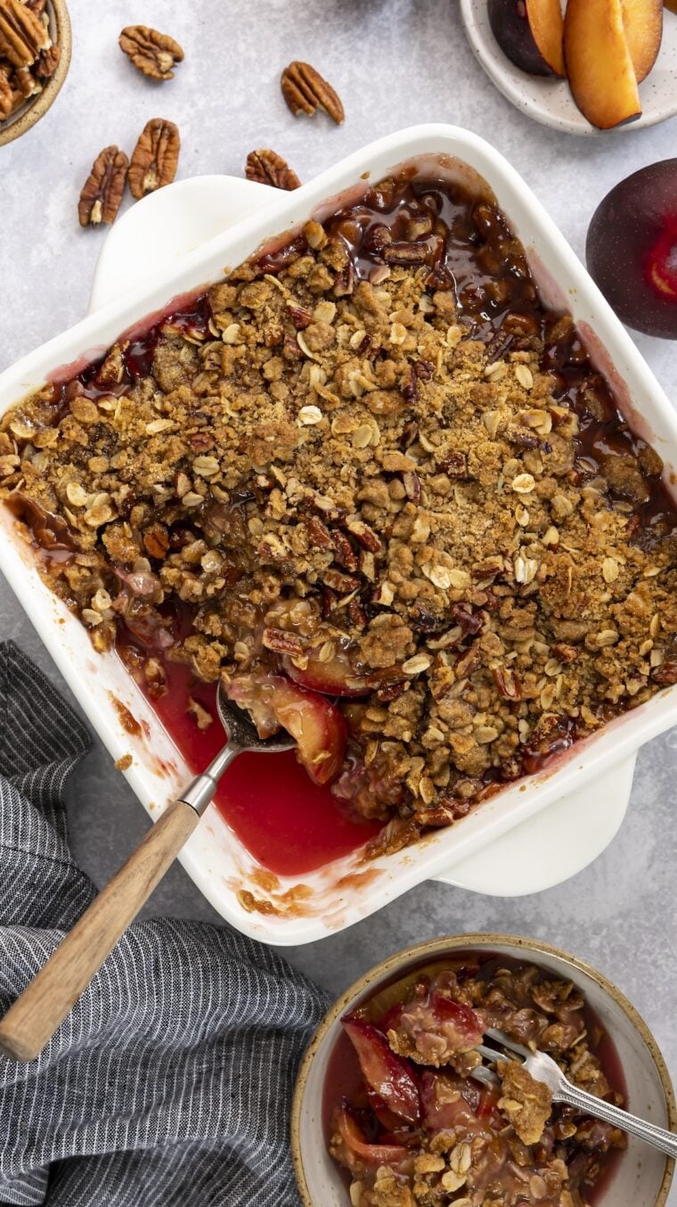 Plum crisp in baking dish with small serving in bowl nearby.