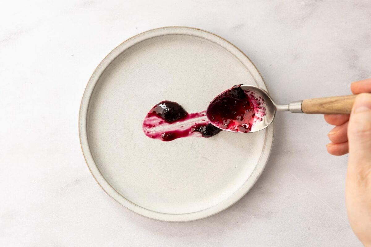 spoon adding streak of blueberry jam to white plate