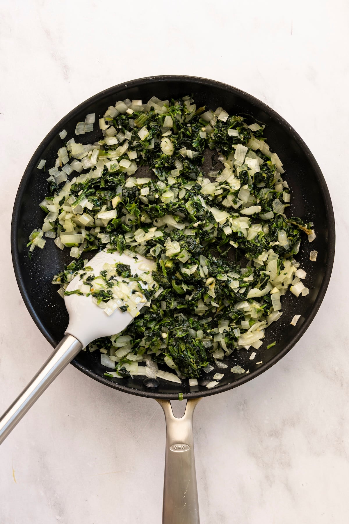 Spinach, onions, and garlic sautéed in skillet.