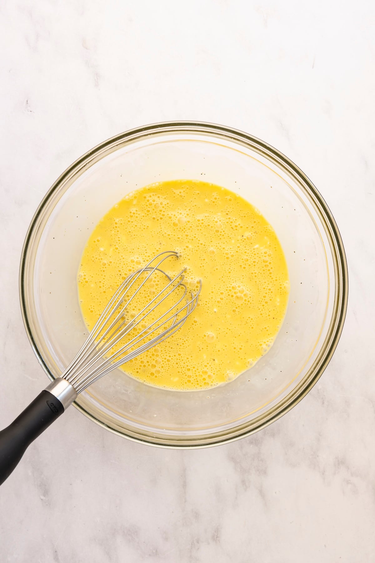 large bowl with eggs, salt, pepper, and heavy cream whisked together