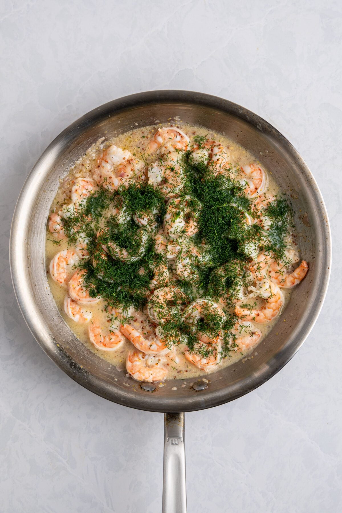 Fresh dill added to the shrimp in the skillet.