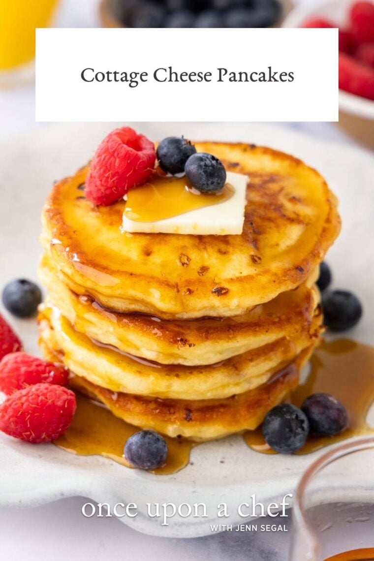white plate with stack of cottage cheese pancakes topped with maple syrup, butter, and berries
