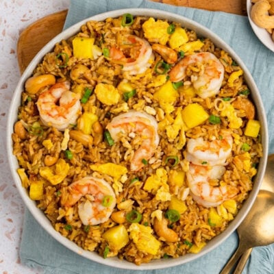 Bowl of pineapple fried rice with small bowls of scallions and cashews.