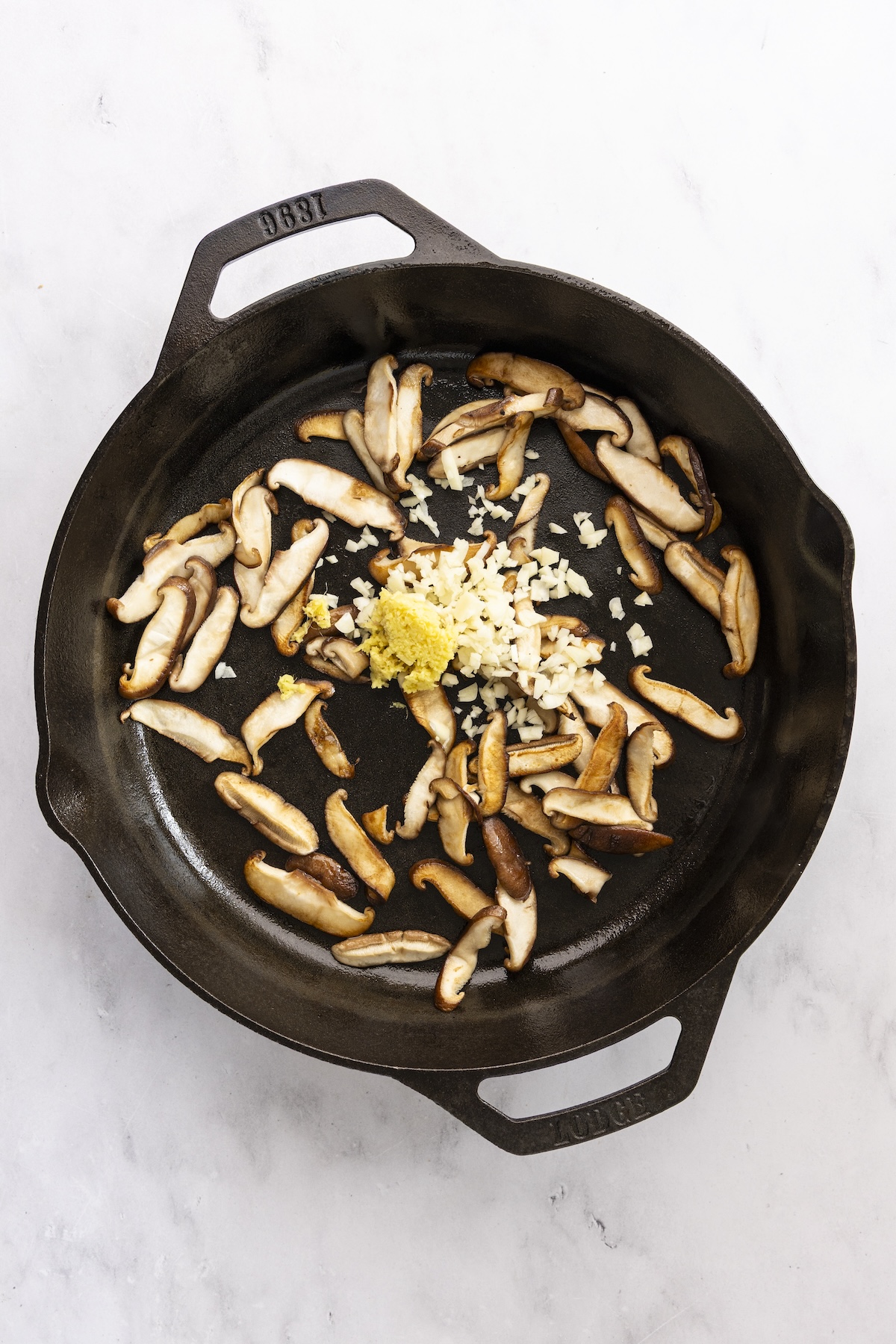 Adding garlic and ginger to cooked mushrooms in skillet.
