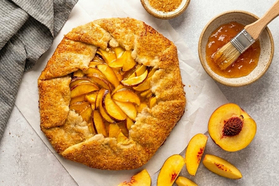 peach galette with bowl of apricot jam glaze.