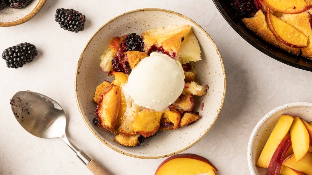 bowl with portion of peach blackberry buckle topped with scoop of vanilla ice cream