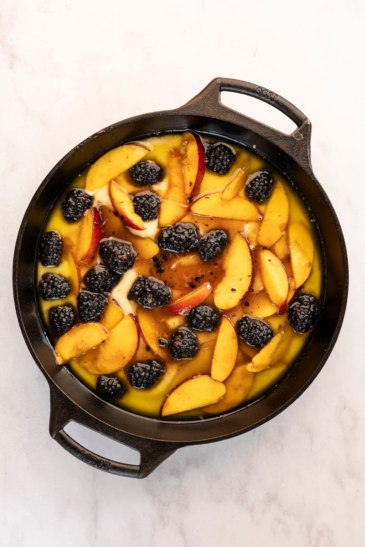 cast iron skillet with peaches and blackberries layered on top of buckle batter