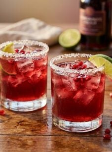 Pomegranate margaritas on wooden table with limes.