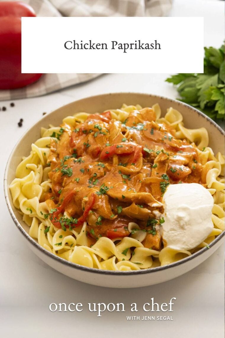 tan bowl with chicken paprikash and dollop of sour cream over buttered egg noodles