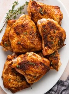 baked chicken thighs on white oval platter garnished with fresh thyme