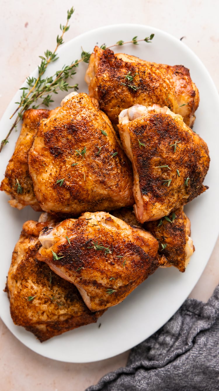 baked chicken thighs on white oval platter garnished with fresh thyme